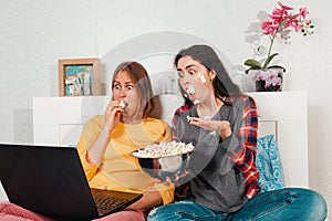 The concept of lesbian relationships. LGBT. Two young women lie together on a bed, eating popcorn and watching a movie on a laptop
