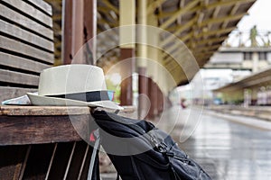 Concept life style holidays travel or journey : Old white hat with black backpack put on the wooden bench at the train station