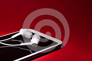 Concept: listen to music from the phone.smartphone with white headphones on a red background