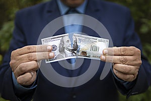 The concept of losing money and income. A businessman in a jacket tears up a paper bill of 100 US dollars. Close-up of