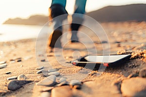 The concept of losing your phone. The smartphone lies on the sand, on the beach. In the background, blurred removing footsteps of