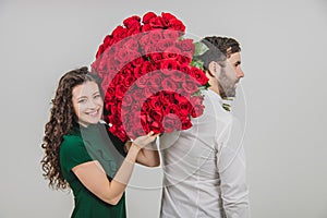 Romantic young man and woman posing with a bouquet of red roses over white background.