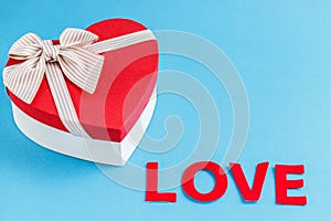 Concept for love stories and for Valentine`s Day. The inscription `Love`, hearts and a box in the form of a heart on a blue backgr