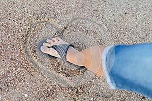 The concept of loveless love and a broken heart. Female foot crushes a heart made of sand