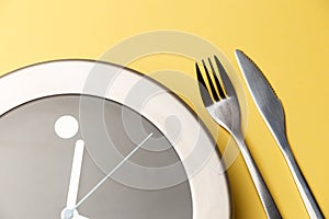The concept of lunch time, meals. Fork with knife and clocks on the colorful yellow background. Time to eat. Top view