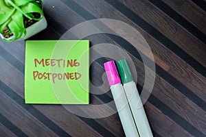 Concept of Meeting Postponed write on sticky notes isolated on Wooden Table