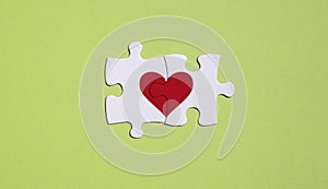 Concept and metaphor of the love union of two people. two white puzzle pieces with a red heart on a green background