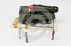 On the dollars is a toy military vehicle, next to the figures of businessmen.