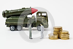 On a white surface are figurines of people, coins and a toy military vehicle.