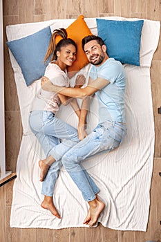 Young adult woman and man lying on bed together and smiling wide