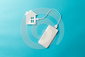 The concept of a modern autonomous smart home. The power bank is connected to the house on blue background