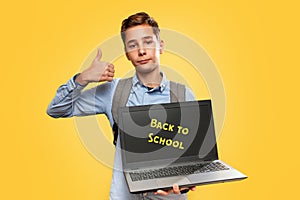 Concept of modern technologies and education. Caucasian teen boy holding open laptop and showing thumbs up. Yellow background.