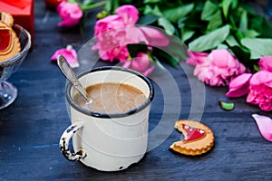 The concept of morning coffee in a romantic style on the black wooden background. Peonies flowers and petals, cookies, heart candl