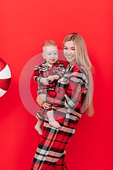 The concept of motherhood. Beautiful young woman and smiling cute baby son in family look on red background with