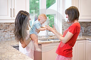 The concept of motherhood, nanny, infancy and childhood. Indoor shot in the kitchen. Two women and a baby in their arms