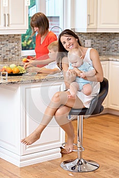 The concept of motherhood, nanny, infancy and childhood. Indoor shot in the kitchen. Two women and a baby in their arms, looking