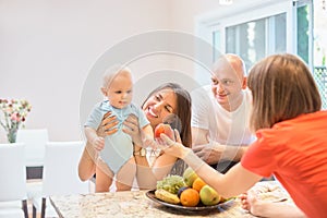 The concept of motherhood, nanny, infancy and childhood. Indoor shot in the kitchen. Two women and a child in their arms, the