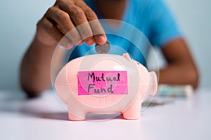 Concept of mutual fund investment, showing with hands placing coins inside the piggy bank with mutual fund sticker