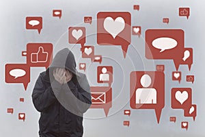 A concept of the negative effects of social media. A hooded man holding his head in his hands. With social media icons surrounding