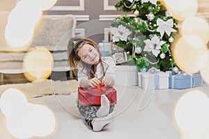 Light photo of cute kid sitting with gift in hands, like a little gnome in christmas decorated room.