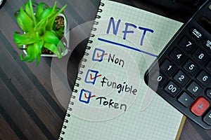 Concept of NFT - Non Fungible Token write on a book isolated on Wooden Table