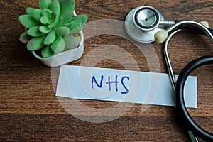 Concept of NHS write on sticky notes with stethoscope isolated on Wooden Table photo