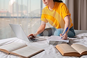 The concept of online courses and online education. A woman is sitting on a bed and working on a laptop. Close up