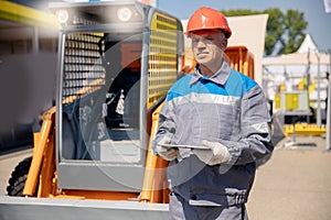 Concept of online internet technologies in construction. Senior worker forklift driver checks route plan on tablet