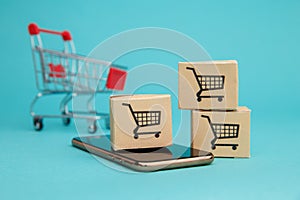 Concept of online Shopping. Boxes and shopping cart above smartphone isolated on blue background