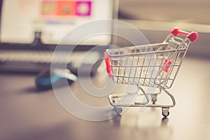 Concept of online shopping: Little shopping cart and a laptop in the blurry background