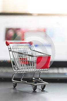 Concept of online shopping: Little shopping cart and a laptop in the blurry background