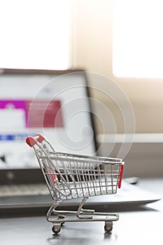 Concept of online shopping: Little shopping cart and a laptop in the blurry background