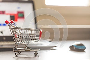 Concept of online shopping: Little shopping cart and a laptop in the blurry background