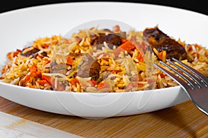 The concept of Oriental cuisine. National Uzbek pilaf with lamb meat in a white plate on a black background. Popular traditional