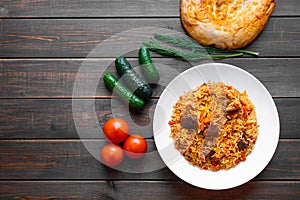 The concept of Oriental cuisine. Traditional Uzbek pilaf with lamb or beef meat on a wooden table with cucumbers, tomatoes and