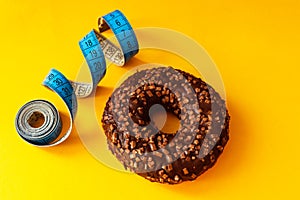 Concept of overweight and weight control. Unhealthy food. Chocolate glazed donut with sprinkles and a measuring tape, metric rules