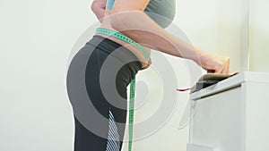 The concept of overweight and weight loss. A woman measures herself with a measuring tape in the bedroom. Looking at