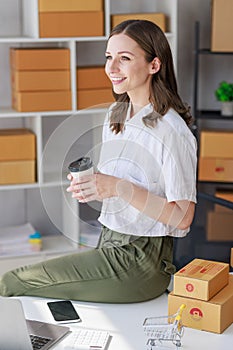 Concept of parcel delivery and selling online,Retailer holding coffee cup feel happy after check sales for the day on online store