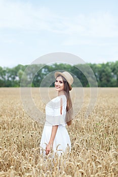The concept of peace of mind. An attractive young woman walks in a golden wheat field. The girl is looking forward with a slight s