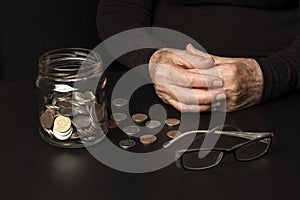 The concept of pension reform. Against the dark background of the hands of an old woman and jar of coins