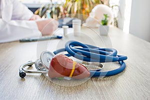 Concept photo of diagnosis and treatment of liver. In foreground is model of liver gallbladder near stethoscope on table in backgr