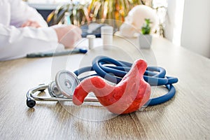 Concept photo of diagnosis and treatment of stomach. In foreground is model of stomach near stethoscope on table in background blu