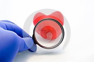 Concept photo of medical examination or diagnosis of heart. Doctor holds in gloved hand magnifying glass, through which one can se