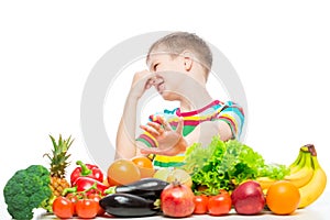 Concept photo of an unloved food - portrait of a boy with an aversion to vegetables and fruits on a white