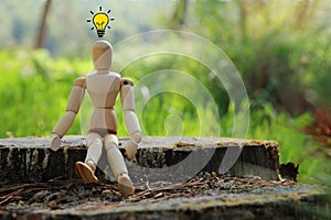 concept photo of wooden dummy sitting outdoors and shiny light bulb. New idea concept or choosing the right solution.