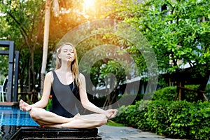 Strong woman sitting in lotus position, doing yoga by the pool on a sunny day