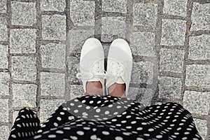 Concept picture of legs walking, Selfie of feet in white sneaker on rock pavement background, top view.