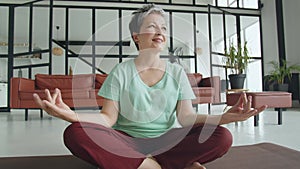 Concept of a pleasant and useful pastime in old age. Old woman make yoga exercise at home. Mature woman have meditation