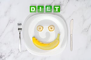 The concept of a positive attitude to diet. Banana on a white plate and the word diet on green wooden cubes