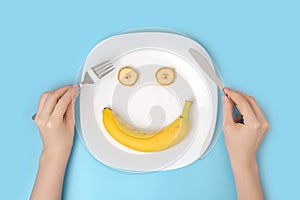 The concept of a positive attitude to diet and healthy eating. Women`s hands with cutlery over a dish with a banana on a blue